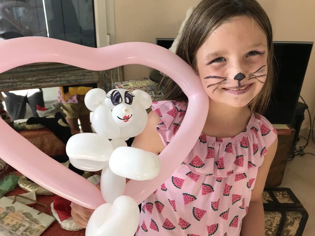 Une enfant souriante avec un cœur et un ourson sculptés en ballons roses et blancs
